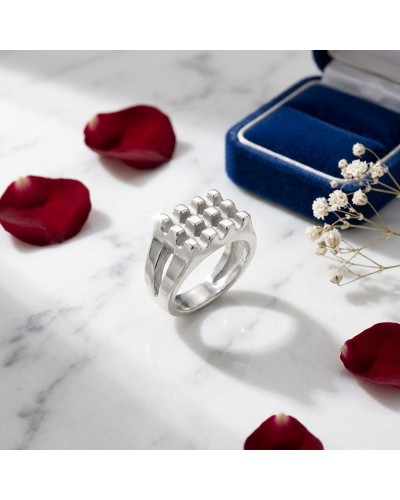 Bague argentée gaussante au design carré gravé, posée sur marbre avec pétales rouges et boîte bleue à côté; nom produit GAUFFRE.