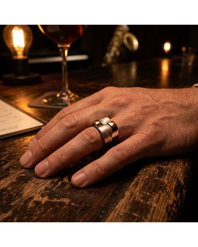 Bague BOSSA NOVA en métal argenté et doré portée sur le dos de la main, posée sur un bar en bois avec verre et lumière chaude.
