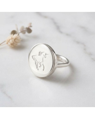 Bague ronde en argent rhodié gravée du logo Murial, sceau circulaire avec motif élégant sur pierre blanche.