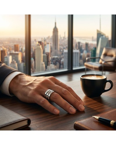 Bague NEW-YORK argentée portée sur le doigt d’un homme, posé sur un bureau en bois avec vue urbaine, café et carnet à proximité.