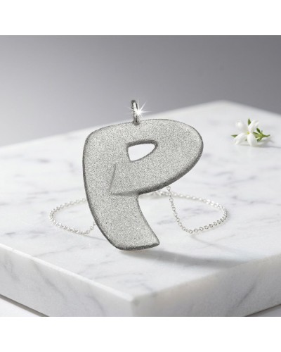 Pendentif argenté en forme de lettre P, texture scintillante, chaîne argentée, posé sur une surface marbrée. Product: Pendentif