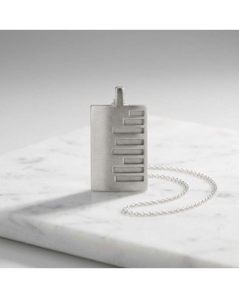 Pendentif rectangulaire argenté avec motif de barres horizontales, chaîne fine, posé sur marbre. Pendentif KEKAYAAN. Chaîne offe