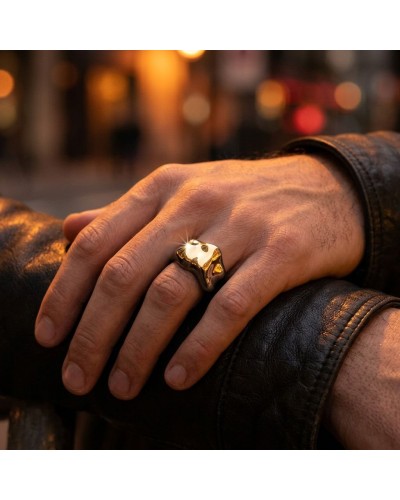 Bague dorée épaissie en forme de tête d’animal sur le doigt, portée sur une main posée sur une veste en cuir, fond urbain flou.