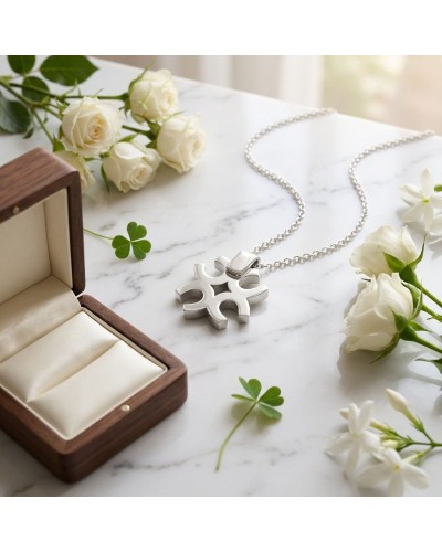 Pendentif en forme de trèfle à quatre branches en argent rhodié avec chaîne, posé près d’une boîte à bijoux et de roses blanches