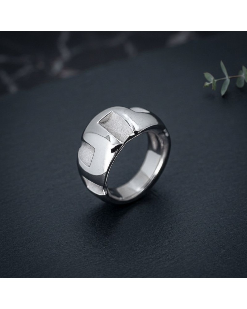 Bague GREC en acier argenté, design moderne à facettes géométriques, portée sur fond sombre.