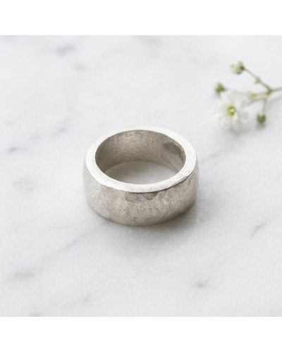 Bague ANNEAU en argent martelé, vue de dessus sur un plan marbré avec petites fleurs en arrière-plan.