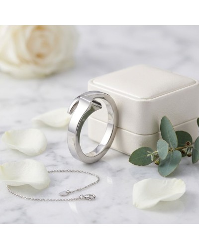 Bague femme en argent rhodié brillante près d’un boîtier crème, chaîne fine et pétales blancs sur marbre.