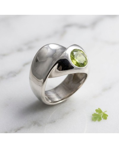 Alliance VRILLE en argent avec péridot vert facetté, bague large et moderne sur marbre.
