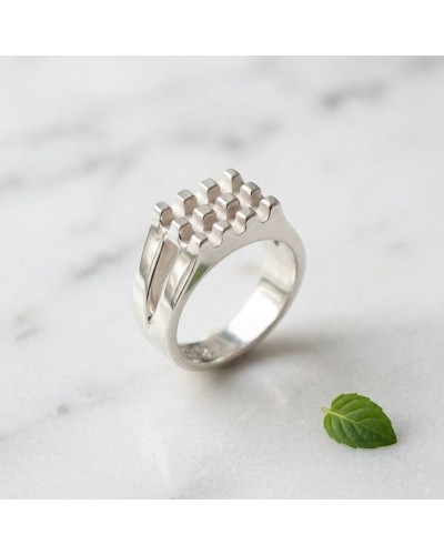 Alliance GAUFFRE femme en or: bague argenté avec motif en relief en forme de carrés, posé sur marbre avec petite feuille verte n