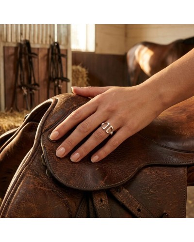 Bague ETRIERS femme en argent rhodié portée sur une main posée sur une selle de cheval en écurie.