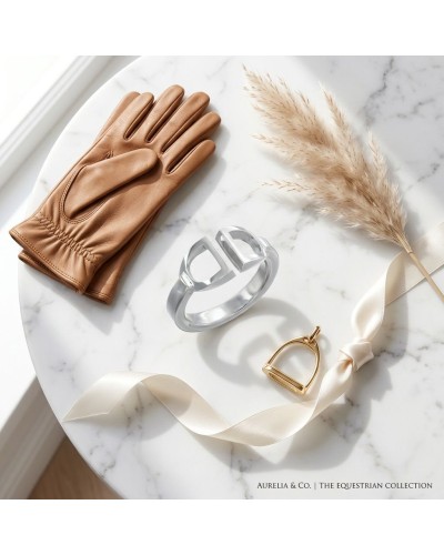 Bague femme en argent rhodié sur table de marbre, entourée de gants cuir beige et d’un ruban blanc décoratif.