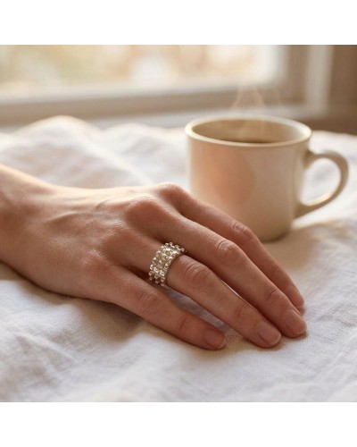 Alliance TEMPS MODERNE femme en or: doigt féminin portant un large anneau argenté à motifs cubes, sur fond de tasse crème.
