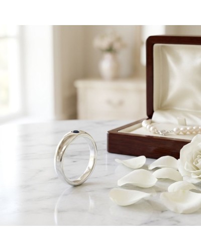 Alliance SOLITAIRE VRILLE femme: bague argentée avec saphir bleu synthétique sur marbre, boîte à bijoux et pétales blancs.