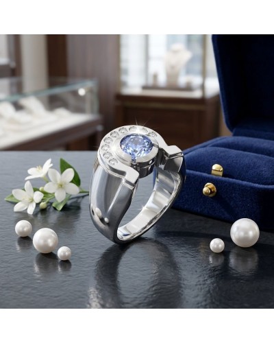 Chevalière en argent rhodié avec saphir synthétique central et diamants blancs surrounding; écrin bleu en velours en arrière-pla