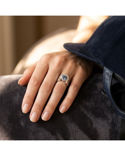 Chevalière en argent rhodié avec saphir synthétique entouré d’oxydes blancs sur un doigt féminin.