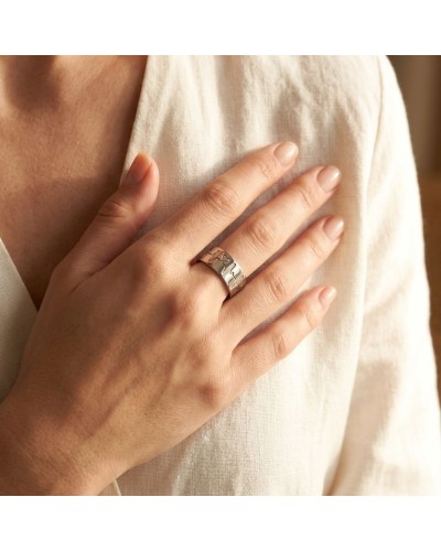 Alliance BEATING LOVE femme en or: doigt portant une bague argentée volumineuse sur une peau nue, près d’un vêtement clair.