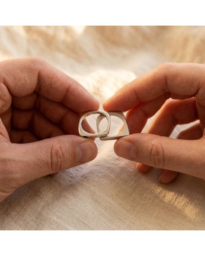 Alliance PYRAMIDE en or sertie d'un saphir bleu - anneaux interlockés entre deux doigts, métal doré et éclat argenté.