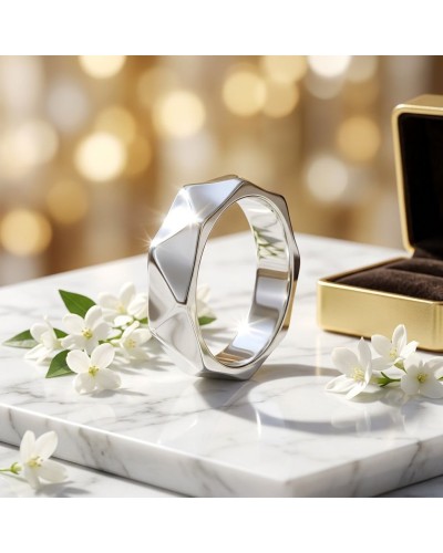 Alliance DRAPE en or: bague géométrique argentée posée sur une surface marbrée, fleurs blanches et boîte dorée en arrière-plan.