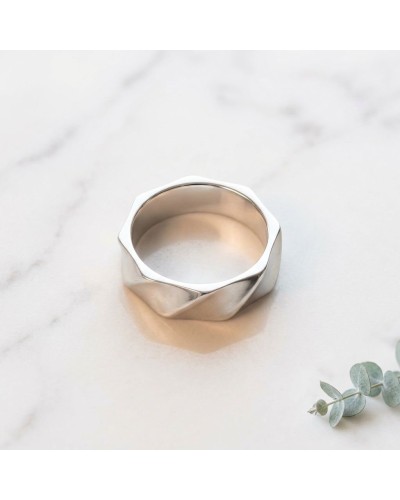 Alliance DRAPE en or : bague argentée au design géométrique, sur pierre blanche marbrée, avec brins de eucalyptus à droite.