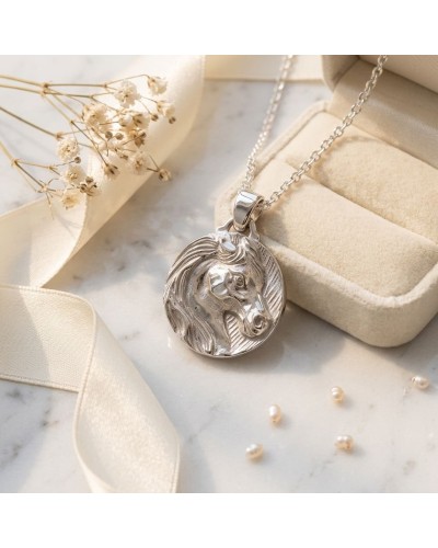 Pendentif médaille ronde en argent rhodié avec motif tête de cheval, sur chaîne près d’un écrin beige et rubans. Médaille ATIANA