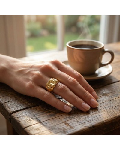 Alliance Tempete femme en or: main féminine posée sur une table en bois, porte une large bague dorée distinctive près d’une tass