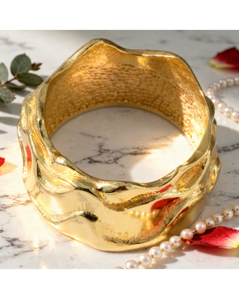 Alliance TEMPETE femme en or: bracelet doré texturé avec motifs ondulés sur fond clair marbré, posé aux côtés de perles et pétal