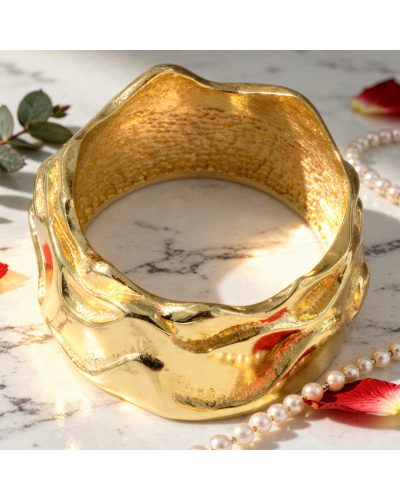 Alliance TEMPETE femme en or: bracelet doré texturé avec motifs ondulés sur fond clair marbré, posé aux côtés de perles et pétal