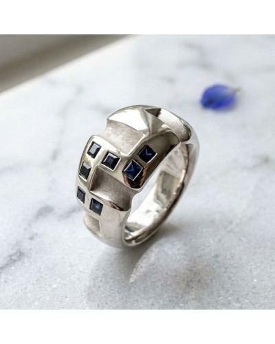Alliance en or sertie de 7 saphirs bleus synthétiques, forme géométrique moderne sur bague argentée.