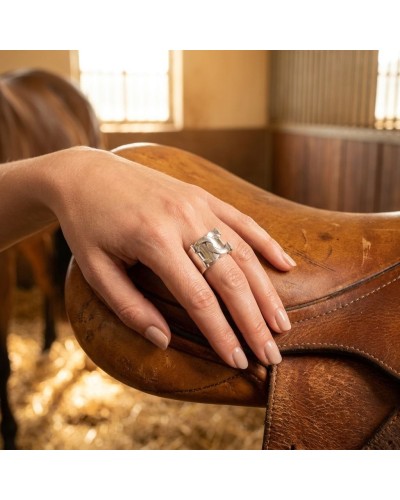 Main sujet: Bague MARECHAL en argent rhodié posée sur une selle en cuir, doigt féminin visible, lumière chaude.