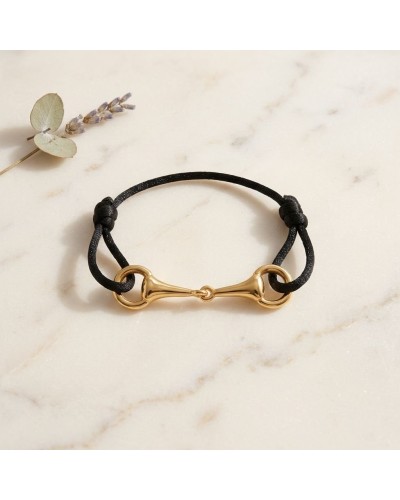 Bracelet MORS en vermeil avec cordon noir, fermoir en forme de mors doré posé sur une plaque pierreuse.