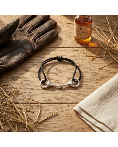 Bracelet MORS en argent rhodié avec cordon noir, posé sur planches en bois près d’un flacon d’huile et d’un gant en cuir.