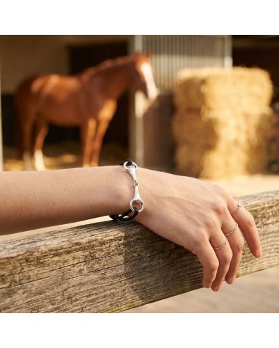 Bracelet MORS en argent rhodié autour du poignet, en métal argenté, avec cuir noir, sur fond de ferme et cheval en arrière-plan.