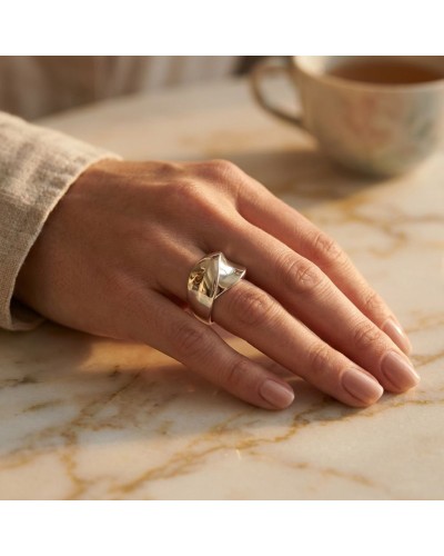 Alliance dorée pour femme portée sur doigt, sur une table en marbre avec tasse floue en arrière-plan.