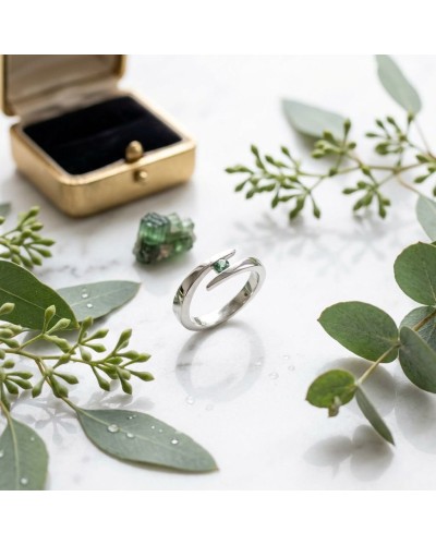 Alliance CROISADE en or avec tourmaline verte sur fond clair, entourée de feuilles et d’une boîte à bijoux ouverte.