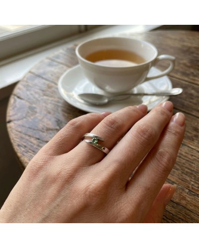 Alliance CROISADE en or avec tourmaline verte sertie sur une bague double tour, portée sur le doigt près d'une tasse de thé.