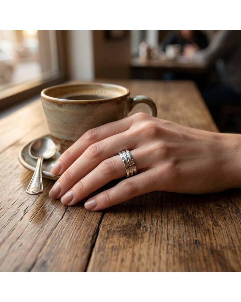Alliance BARK pour femme en or: doigt portant deux bagues argentées sur fond de tasse à café sur table en bois.