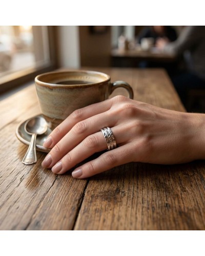 Alliance BARK pour femme en or: doigt portant deux bagues argentées sur fond de tasse à café sur table en bois.