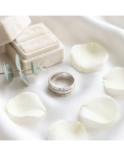 Alliance BARK pour femme en or: bague argentée avec motif texturé, entourée de pétales blancs et eucalyptus sur fond blanc.
