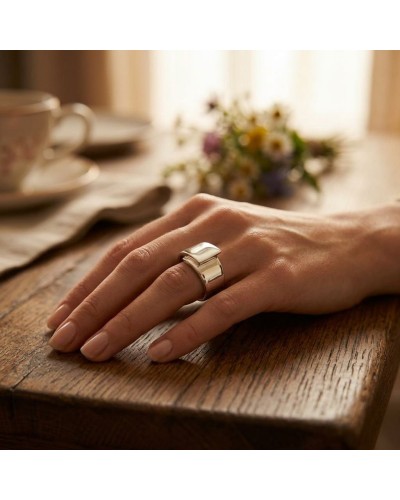 Alliance TOI SUR MOI pour femme en or: doigt portant une bague argenté sur une main posée sur une table en bois, fond flou de fl