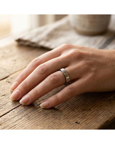 Alliage or jaune avec motif strié porté sur doigt féminin, visible sur une main posée sur bois.