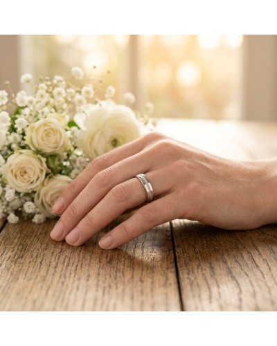 Alliance intérieur sablé pour femme en or: doigt portant double bague argent, bouquet blanc en arrière-plan.