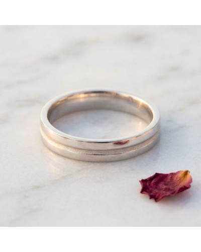 Alliance intérieur sablé pour femme en or: bague double ridée, lustrée dorée, posée sur marbre avec pétale sèche.