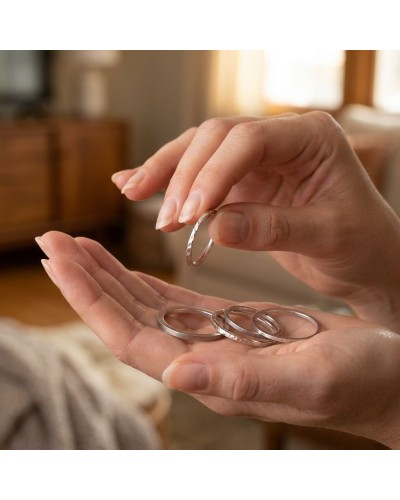 Alliance à effet de matière pour femme en or: une main tient une bague argentée texturée, avec d'autres anneaux posés sur l'autr