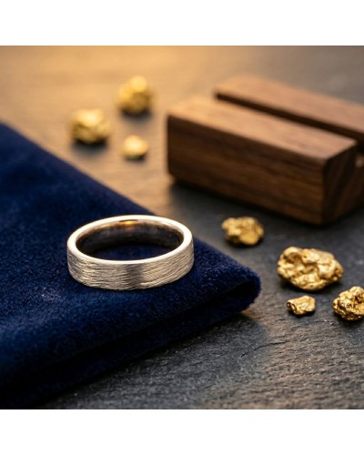 Alliance homme en or effet griffé posée sur un tissu bleu foncé avec petits galets dorés et bois en arrière-plan.