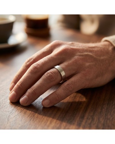 Alliance homme en or argenté posé sur doigt sur table, bracelet plat, style minimaliste pour homme.