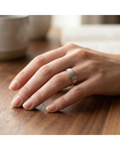 Alliance effet brossé pour femme en or sur doigt, prise de main posée sur table en bois.