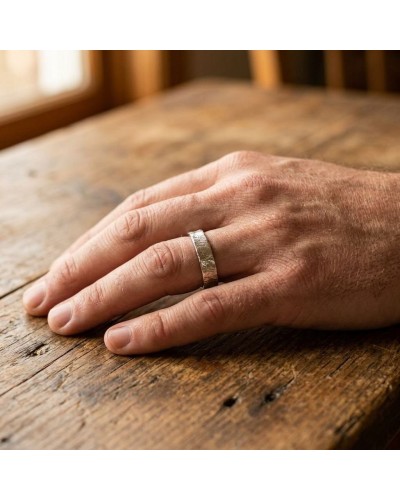 Alliance homme en or effet crayonné sur doigt posé sur table en bois, mise en valeur du anneau chic.