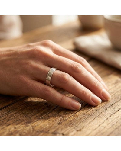 Alliance effet crayonné pour femme en or: bague argentée à motif texturé portée sur le doigt.