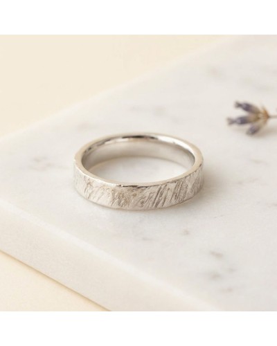 Alliance effet crayonné pour femme en or - bague argentée à texture crayonnée posée sur marbre, fleur floue en arrière-plan