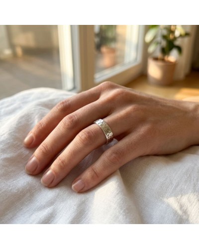 Alliance effet martelé pour femme en or portée sur le doigt, bijoux élégant près d’une fenêtre.